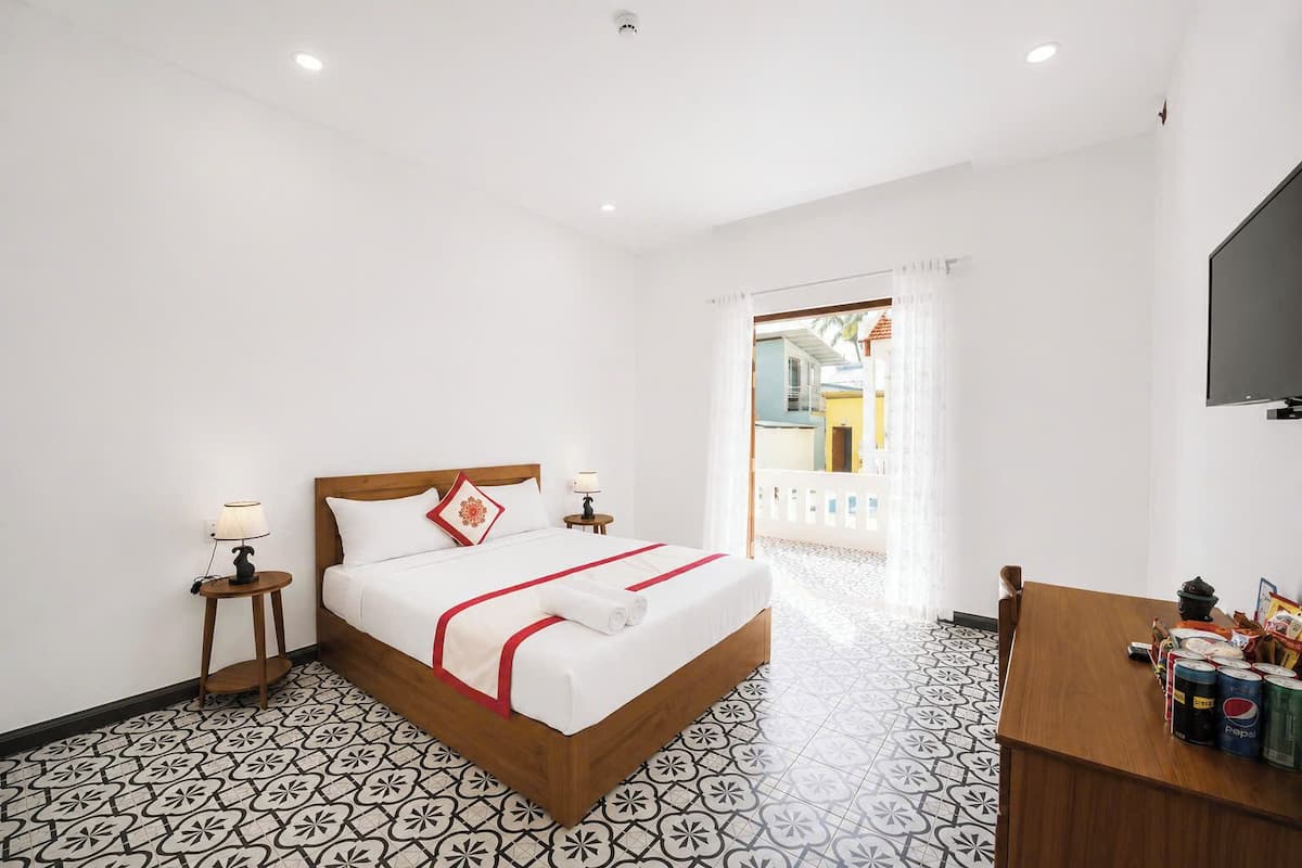 A hotel room with a bed, two bedside tables with lamps, a TV mounted on the wall, and a dining table with Pepsi cans.