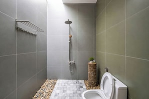 A modern bathroom with a shower, toilet, and a small plant on a wooden stool.