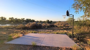 An outdoor basketball court with a metal hoop, surrounded by dry grass and trees. - Cortez RV Resort (Cortez)