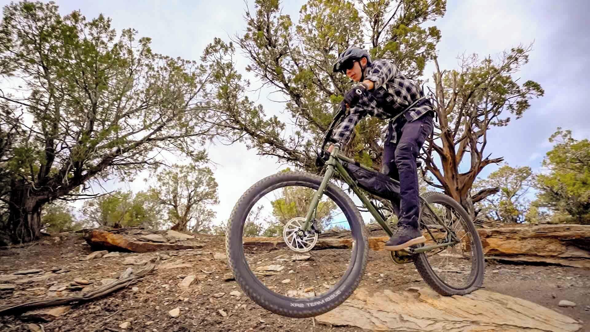 A person riding a mountain bike on a dirt trail with trees in the background.