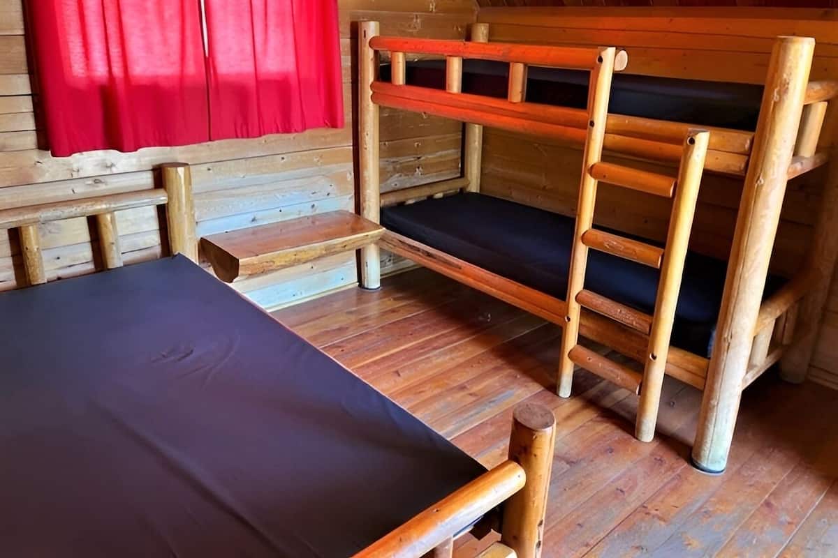A wooden bunk bed with a mattress, a wooden ladder, and a red curtain.