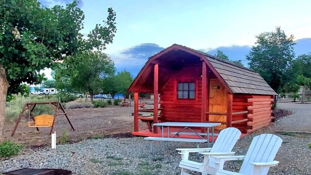 A rustic cabin with a porch, a swing, and two Adirondack chairs. - Cortez RV Resort (Cortez)