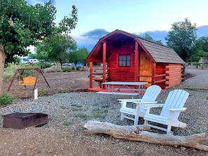 A rustic cabin with a porch, a swing, and two Adirondack chairs. - Cortez RV Resort (Cortez)