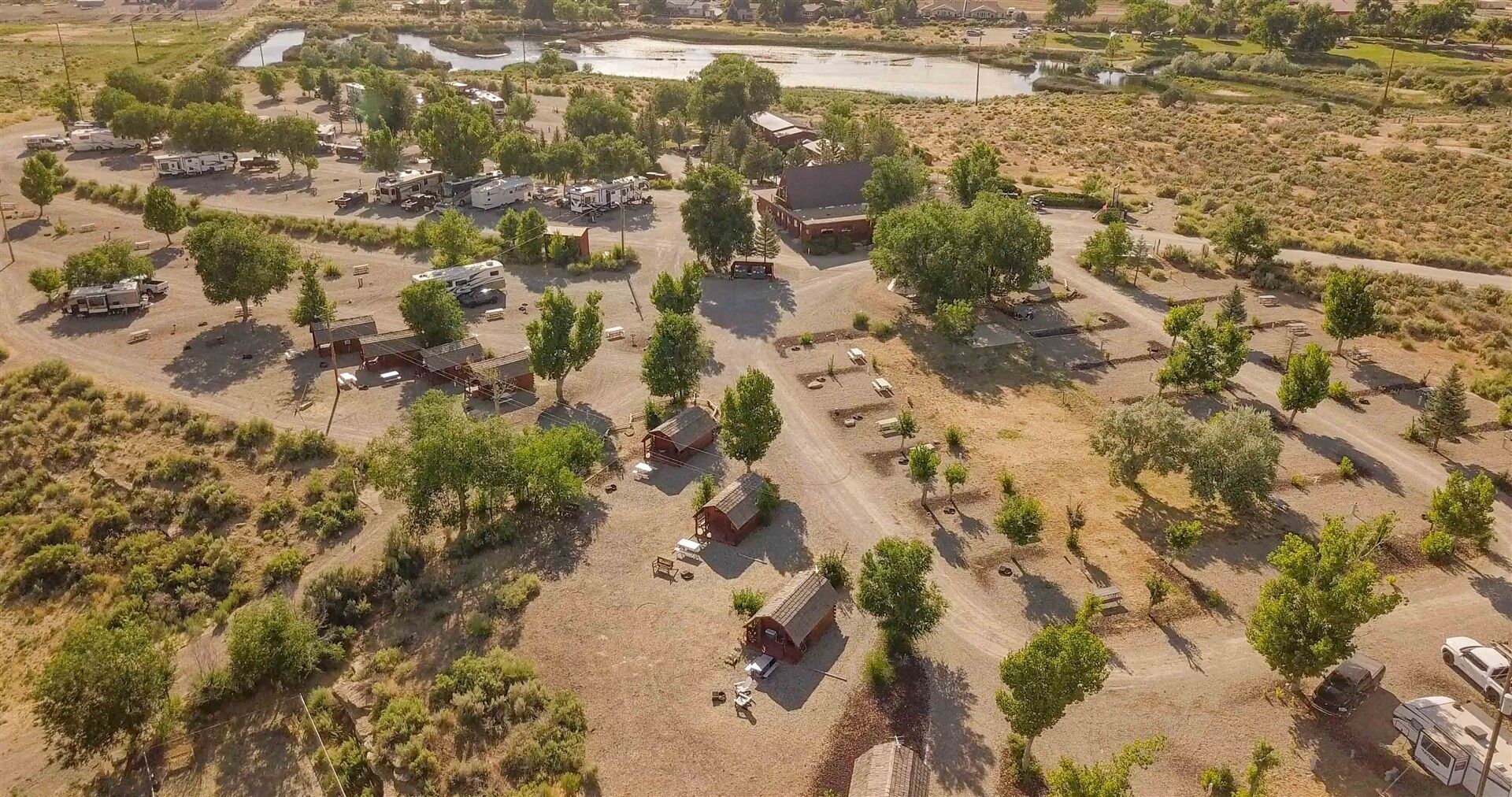 An aerial view of a campground with RVs, small cabins, and a lake.