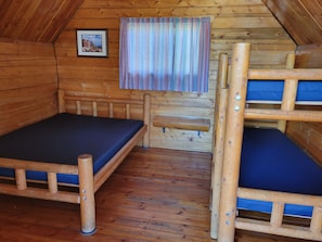 A wooden cabin room with bunk beds, a small window with curtains, and a framed picture on the wall. - Cortez RV Resort (Cortez)