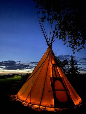 A traditional teepee with a fire inside, set against a twilight sky.