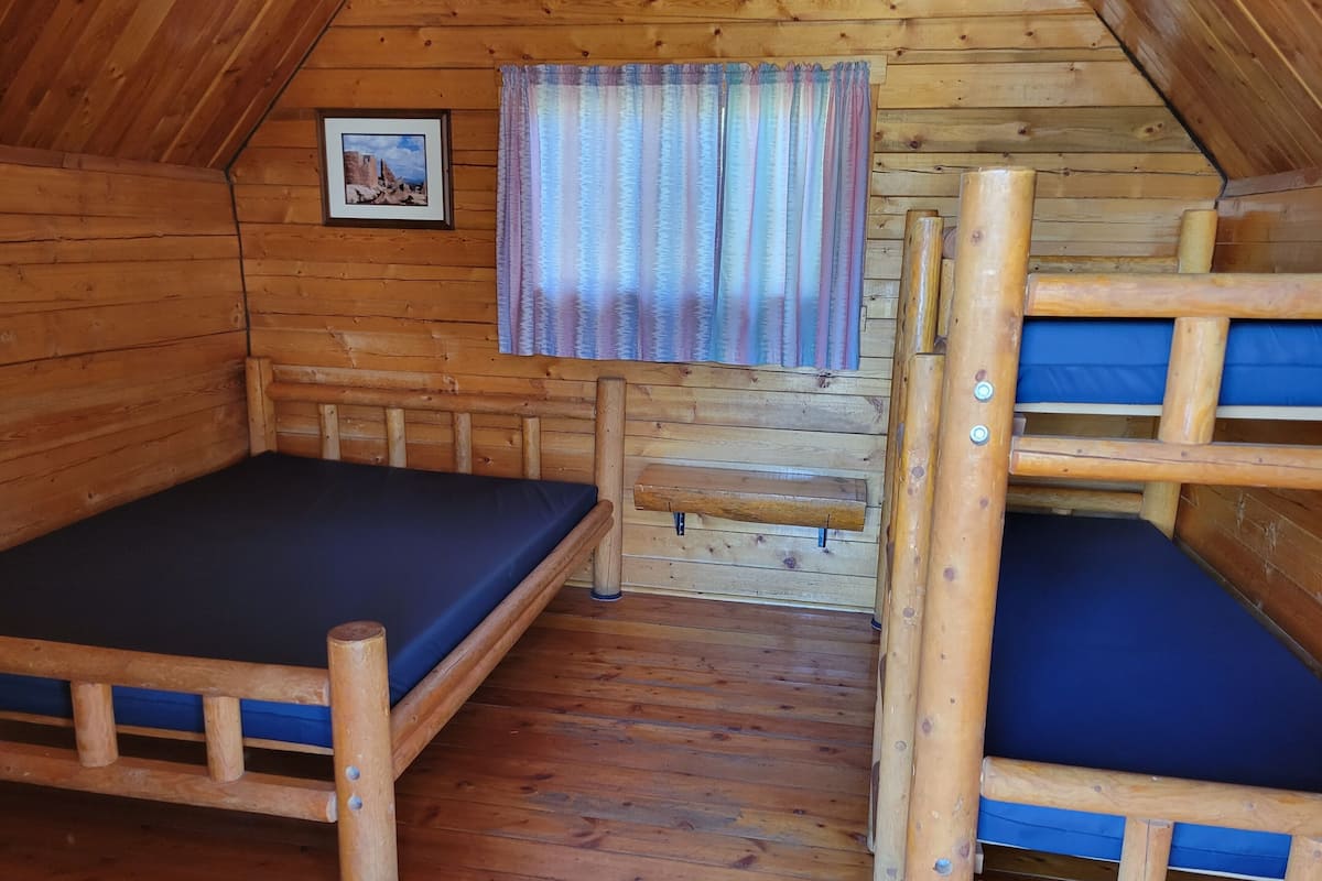 A wooden cabin with bunk beds, a framed picture on the wall, and a window with curtains.