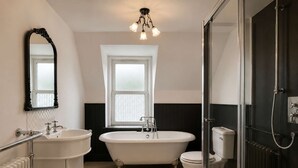 Ein Badezimmer mit freistehender Badewanne, Toilette, Waschbecken mit Spiegel und Duschbereich.