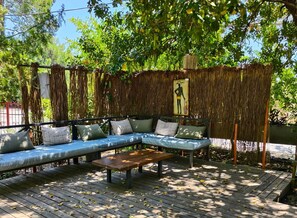 Un espace extĂ©rieur amĂ©nagĂ© avec un canapĂ© et une table, entourĂ© dâun mur en chaume et de verdure.