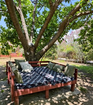 Un banc en bois, recouvert dâune couverture Ă carreaux et agrĂ©mentĂ© de coussins, placĂ© sous un arbre.