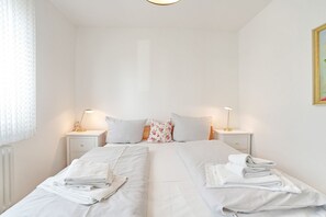 Ein Doppelbett mit weißen Leinen, zwei Nachttische mit Lampen, ein Blumenkissen und ein Bild an der Wand.