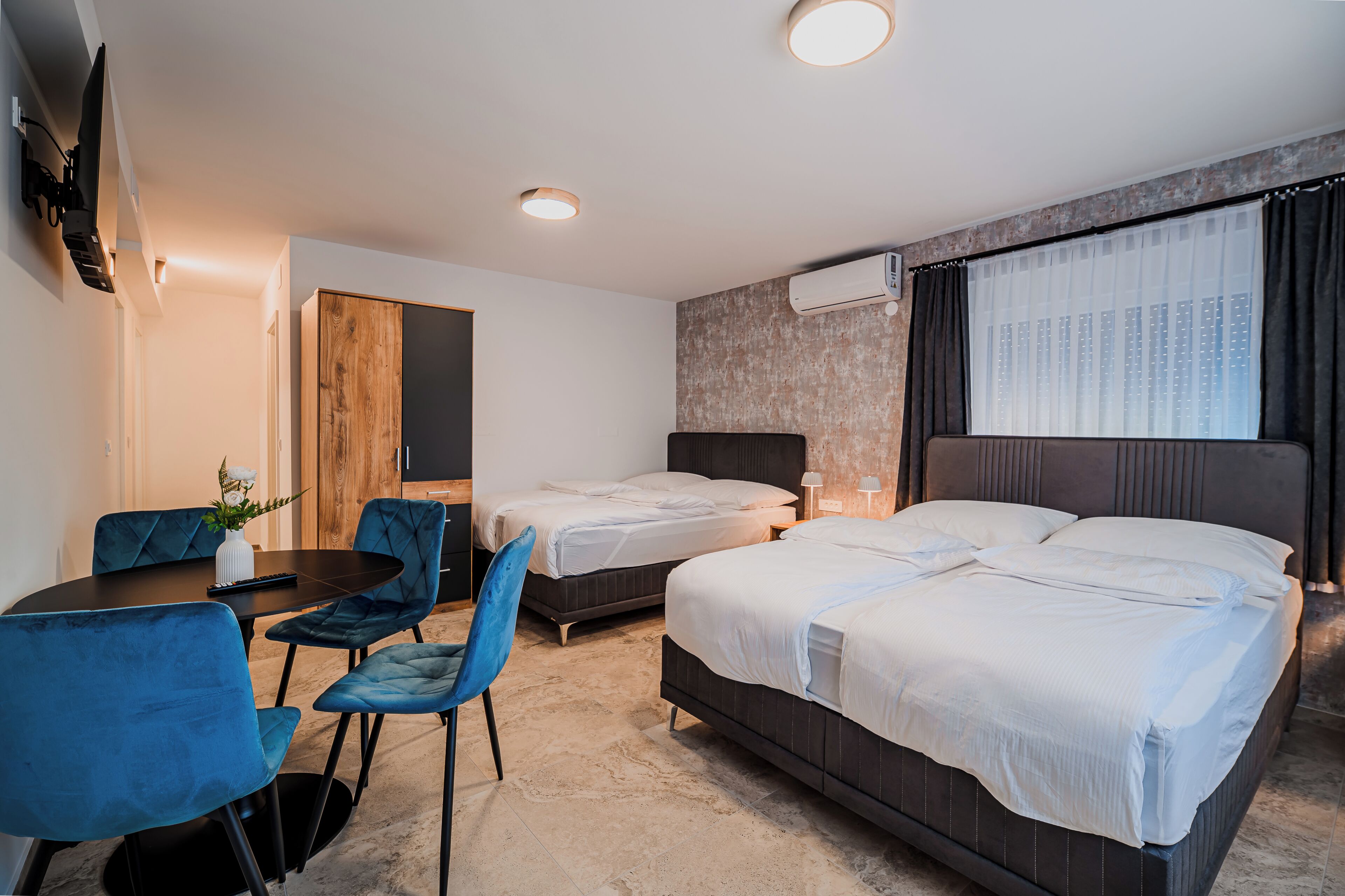 Ein Hotelzimmer mit zwei Betten, einem Schreibtisch mit Stühlen, einem Fernseher und einer Klimaanlage.