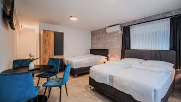 Ein Hotelzimmer mit zwei Betten, einem Schreibtisch mit Stühlen, einem Fernseher und einer Klimaanlage.