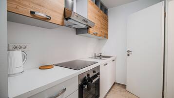 A compact kitchen with white cabinetry, a built-in oven, a stovetop, and a coffee maker.