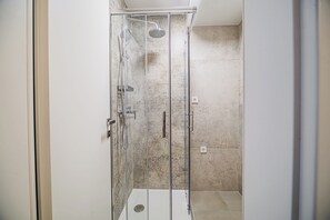 A glass-enclosed shower with a handheld showerhead, a wall-mounted faucet, and a control panel. - Apartment House Barsel (Ljubljana)