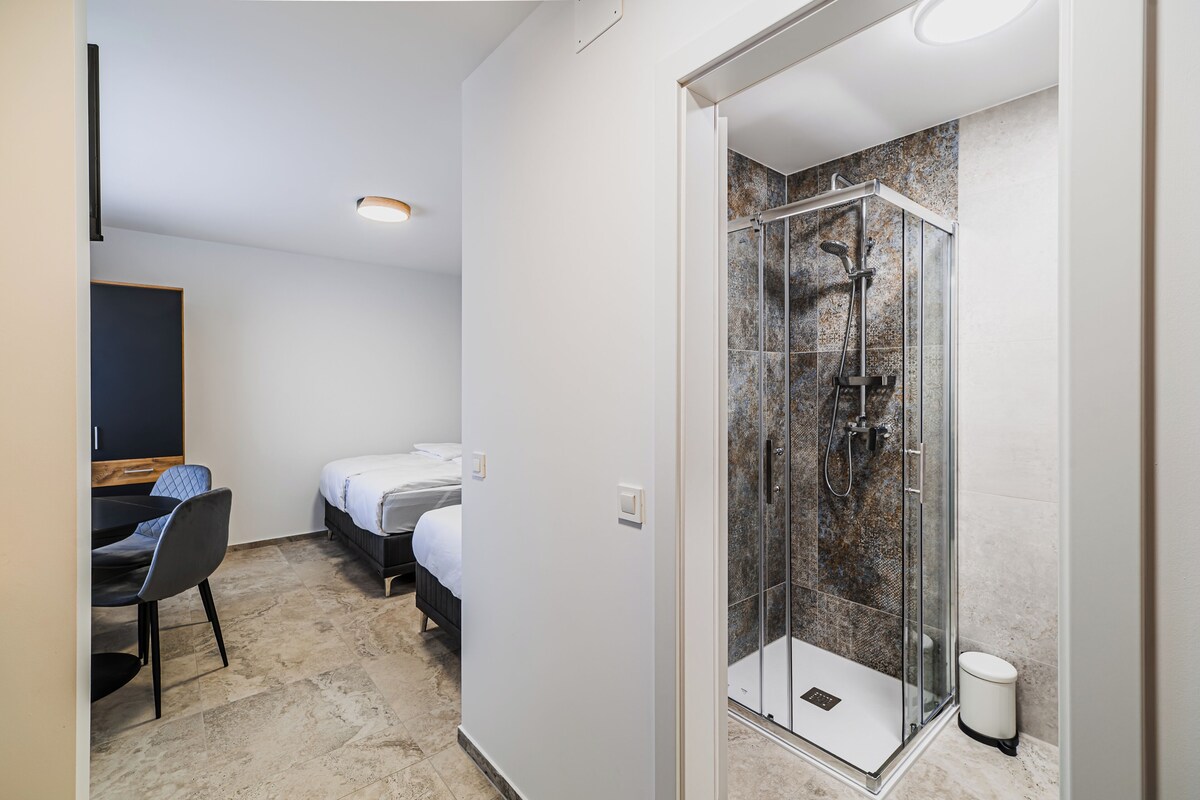 Hotellihuone, jossa on suihku, sänky, työpöytä ja tuoli.