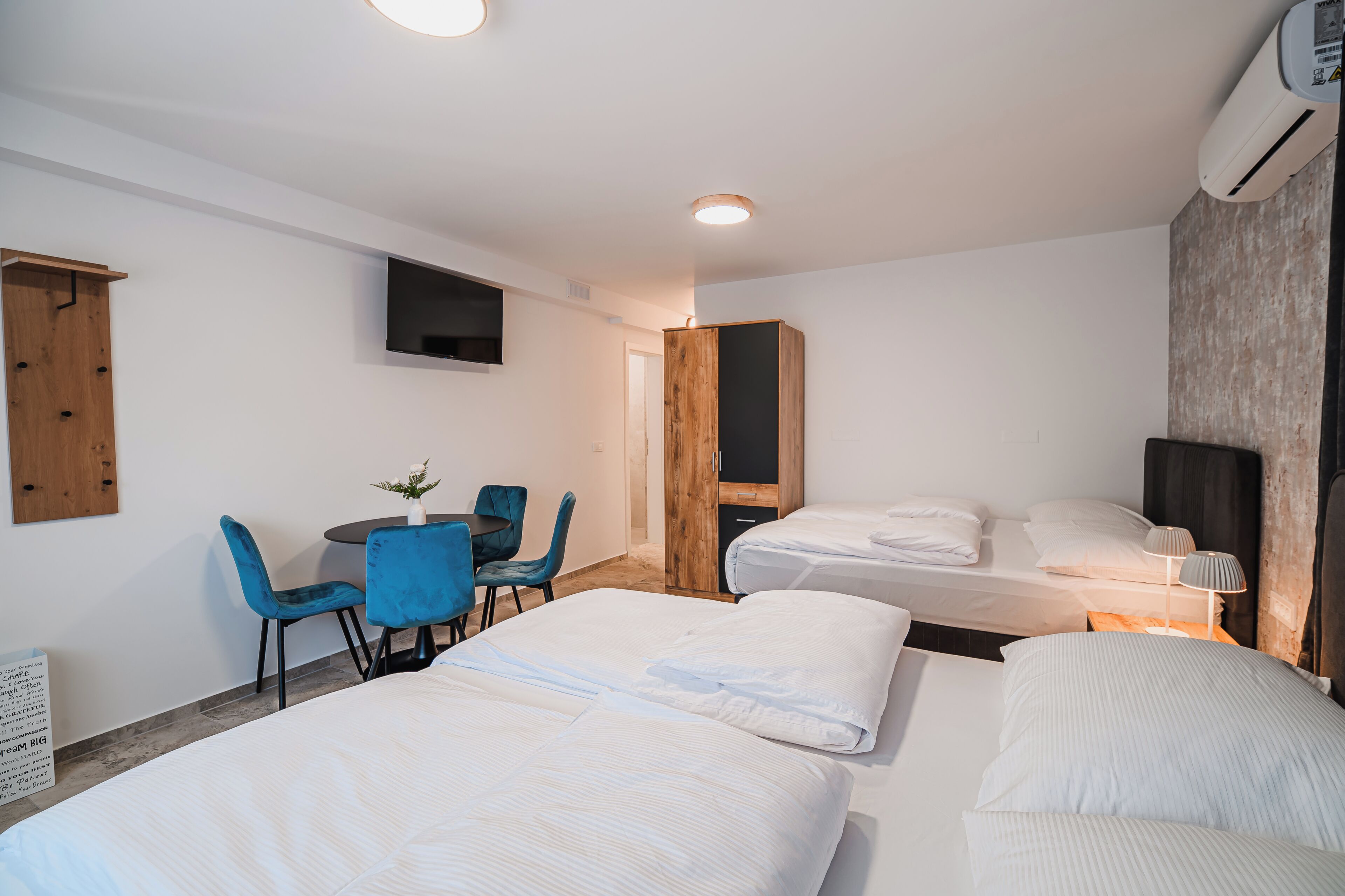 Una habitación de hotel con dos camas, un escritorio con sillas, un televisor y un equipo de aire acondicionado.