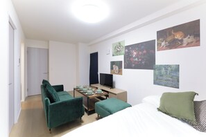 A modern hotel room with a bed, two green sofas, a small table with cups and saucers, a TV, and artwork on the walls. - Mugenzaka by Tranova 2 (Shibuya)