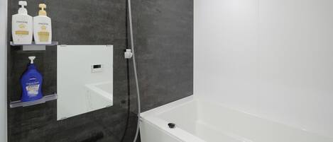 A bathroom with a bathtub, a shower, and a mirror. There are two bottles of Pantene shampoo and a bottle of Hema cream on the shelf.