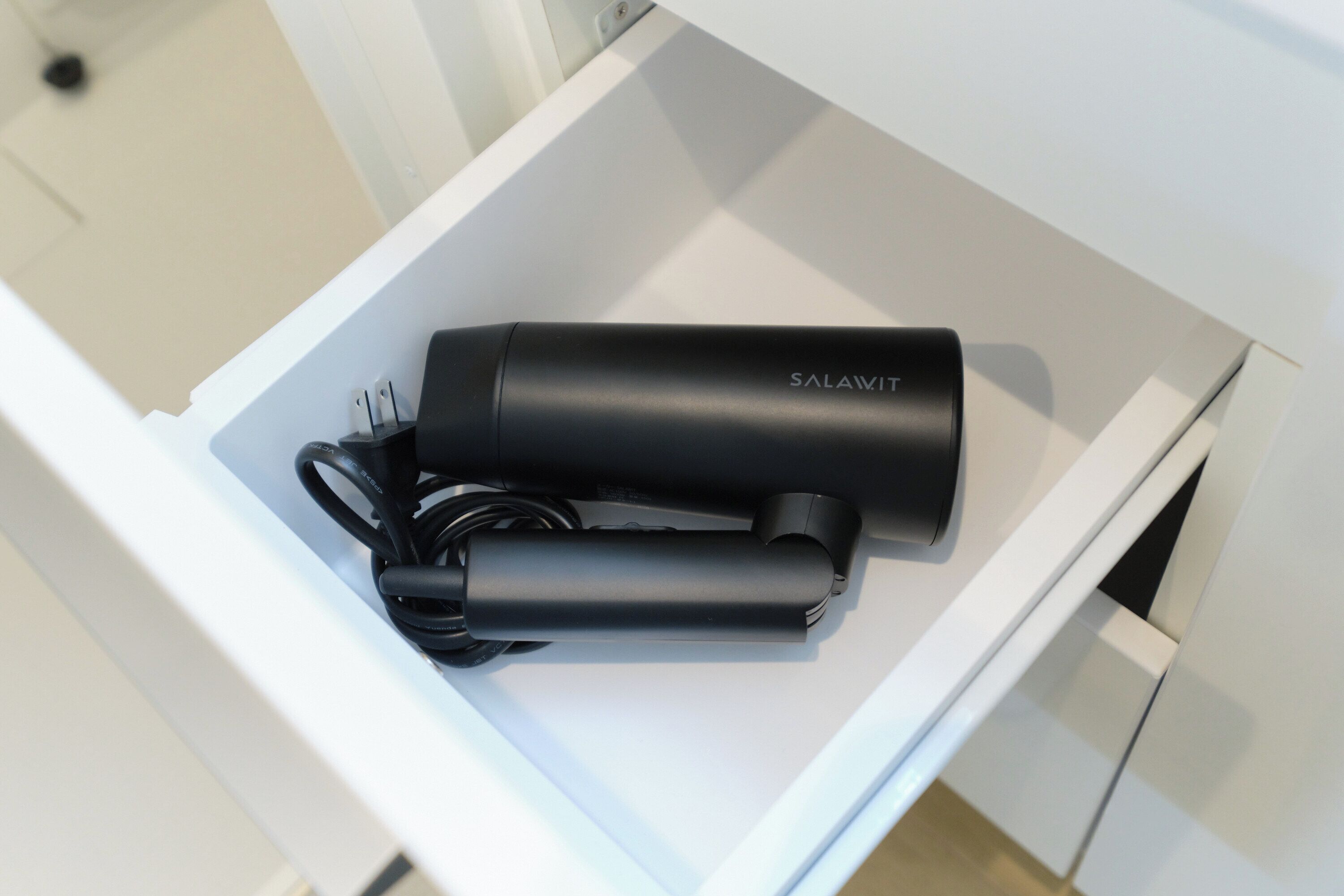 A white drawer containing a black cylindrical object labeled 'SALAWIT' and a coiled black cable.