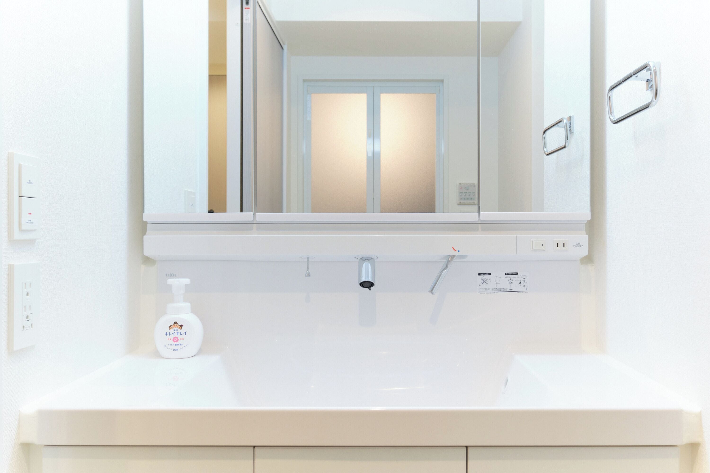 A bathroom with a white sink, a mirror, and a bottle of hand soap.