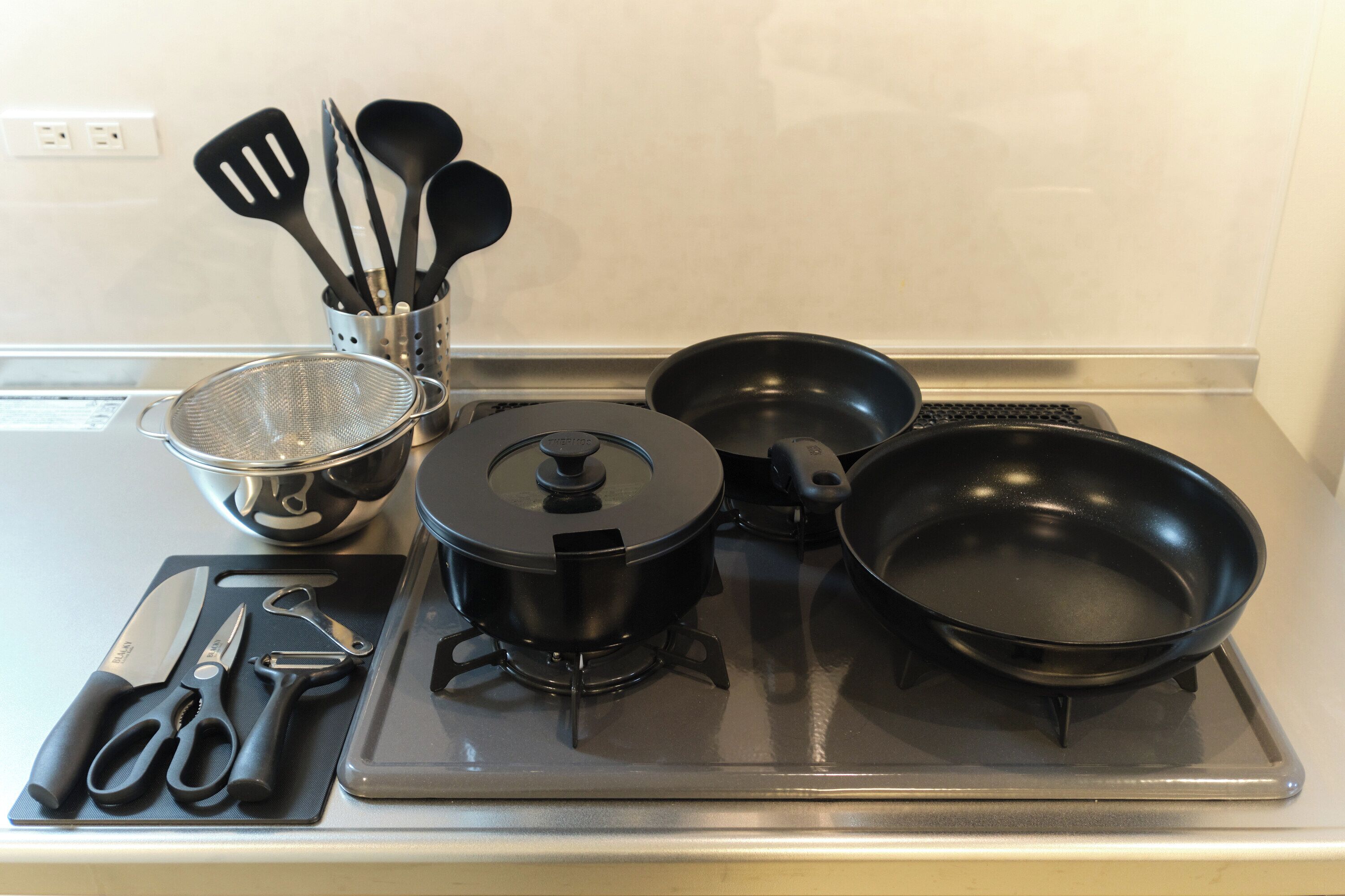 Una cocina con estufa, ollas, sartenes y utensilios.
