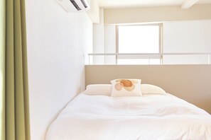 A hotel room with a bed, a window, and a wall-mounted air conditioner. - Liverty Place Nakano 2 (Tokyo)