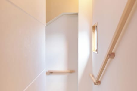 A narrow stairway with a wooden handrail and a small window at the top.