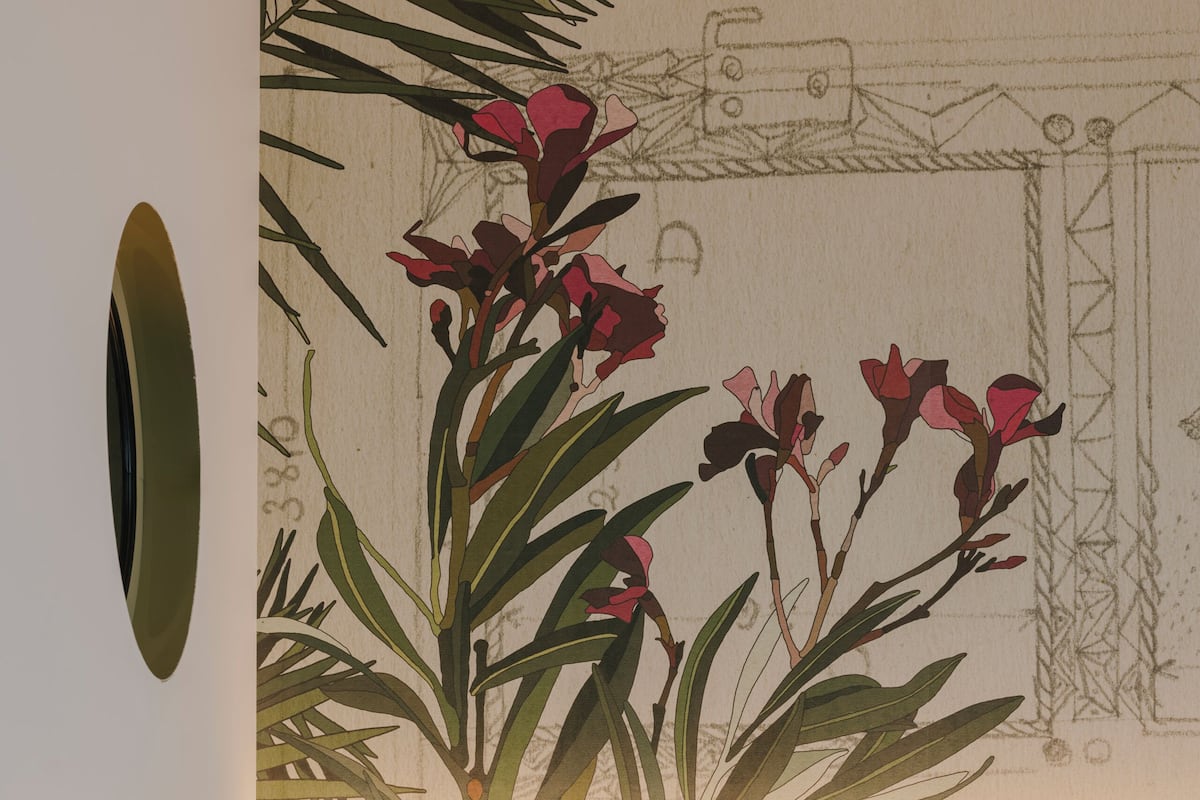 A hotel room with a bed, a nightstand with a lamp and phone, and a wall with a floral mural.