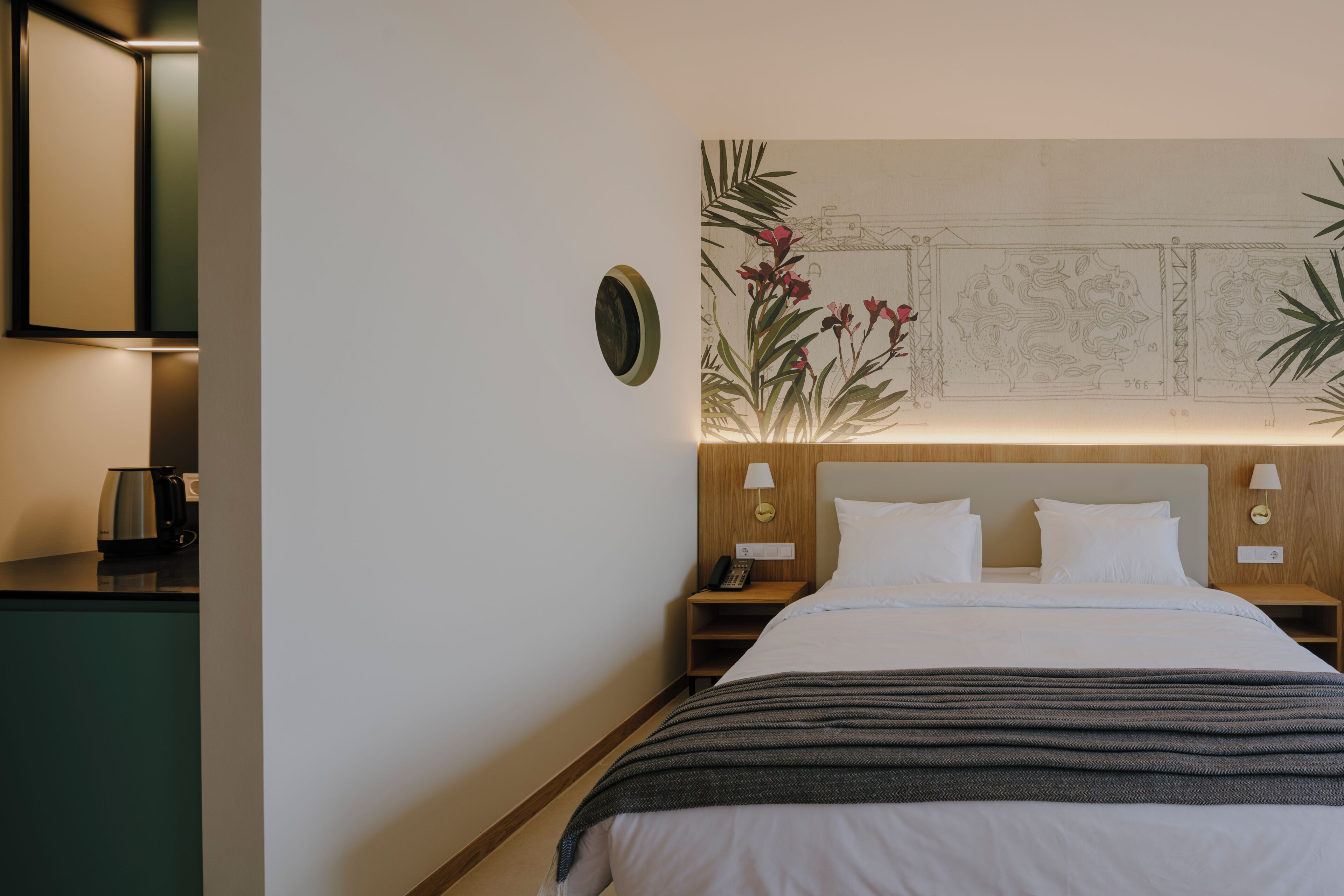 Een hotelkamer met een bed, nachtkastjes, een kunstwerk aan de muur en een koffiezetapparaat op het aanrecht.