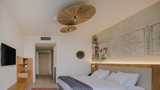 Ein Schlafzimmer mit einem Bett, einer Holzbank, einem roten Teppich mit Muster, einem an der Wand montierten Fernseher und einem Deckenventilator.