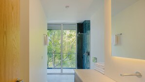 Ein modernes Badezimmer mit einem großen Spiegel, einer Dusche und Blick auf Bäume durch die Glastür.