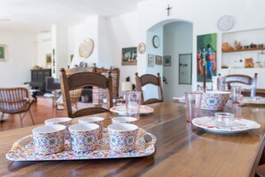 A dining table with a tray of patterned cups and saucers, wooden chairs, and a clock on the wall. - GuestHost - Lovely Sea View Villa with Parking (Porto Columbu-Perd'È Sali)