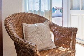 A wicker chair with a cushion, positioned near a window with a view of the outside. - GuestHost - Lovely Sea View Villa with Parking (Porto Columbu-Perd'È Sali)