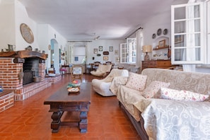 A living room with a fireplace, a sofa, a wooden coffee table, and a dining area with chairs and a table. - GuestHost - Lovely Sea View Villa with Parking (Porto Columbu-Perd'È Sali)