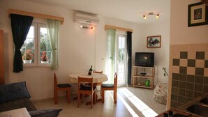 Una sala de estar con sofá, una mesa de comedor con sillas, un televisor y una zona de cocina con fregadero y estufa.