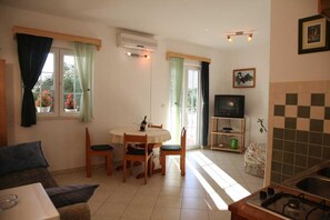 A living room with a sofa, a dining table with chairs, a TV, and a kitchen area with a sink and stove. - Srima Villa Steps from Sandy Beach (Srima)