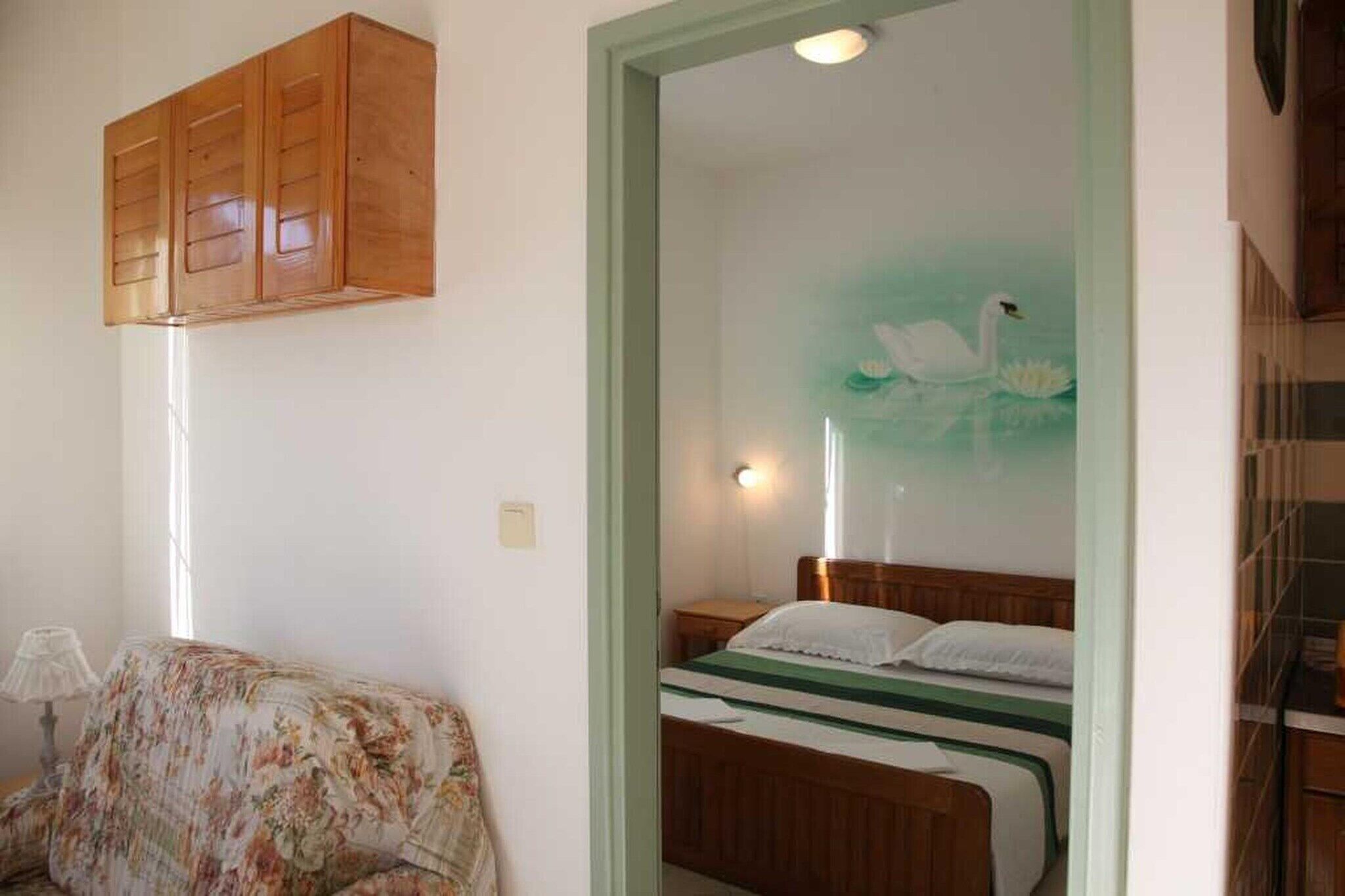Ein Schlafzimmer mit einem Bett, einem Holzschrank, einem blumigen Sofa und einer Wand mit einem Schwanbild.
