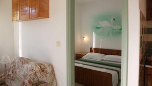 Un dormitorio con una cama, un armario de madera, un sofá floral y una pared con un cuadro de un cisne.