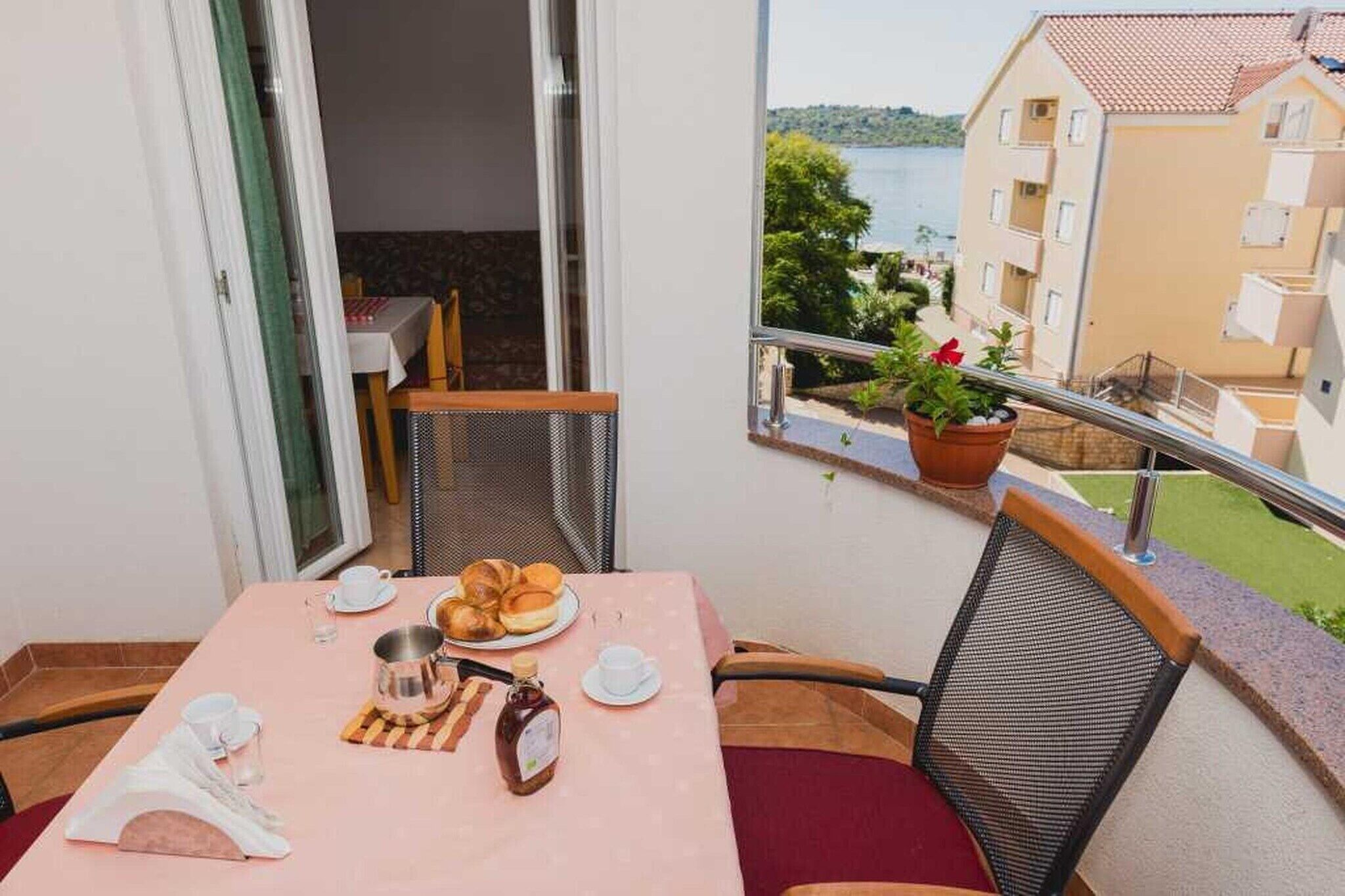 Ein Balkon mit einem Frühstückstisch, Blick auf ein Gebäude und einem Blumentopf.