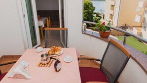 Varanda com mesa posta para o café da manhã, vista de um edifício e um vaso de planta.