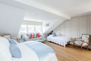 Quarto com teto inclinado, uma cama, uma poltrona, um sofá e uma janela.