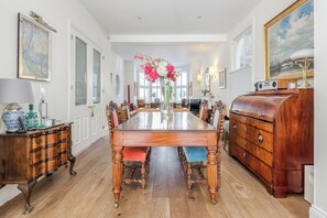 Uma sala de jantar com uma mesa de madeira, cadeiras, um vaso de flores, um armário de madeira e um quadro na parede.