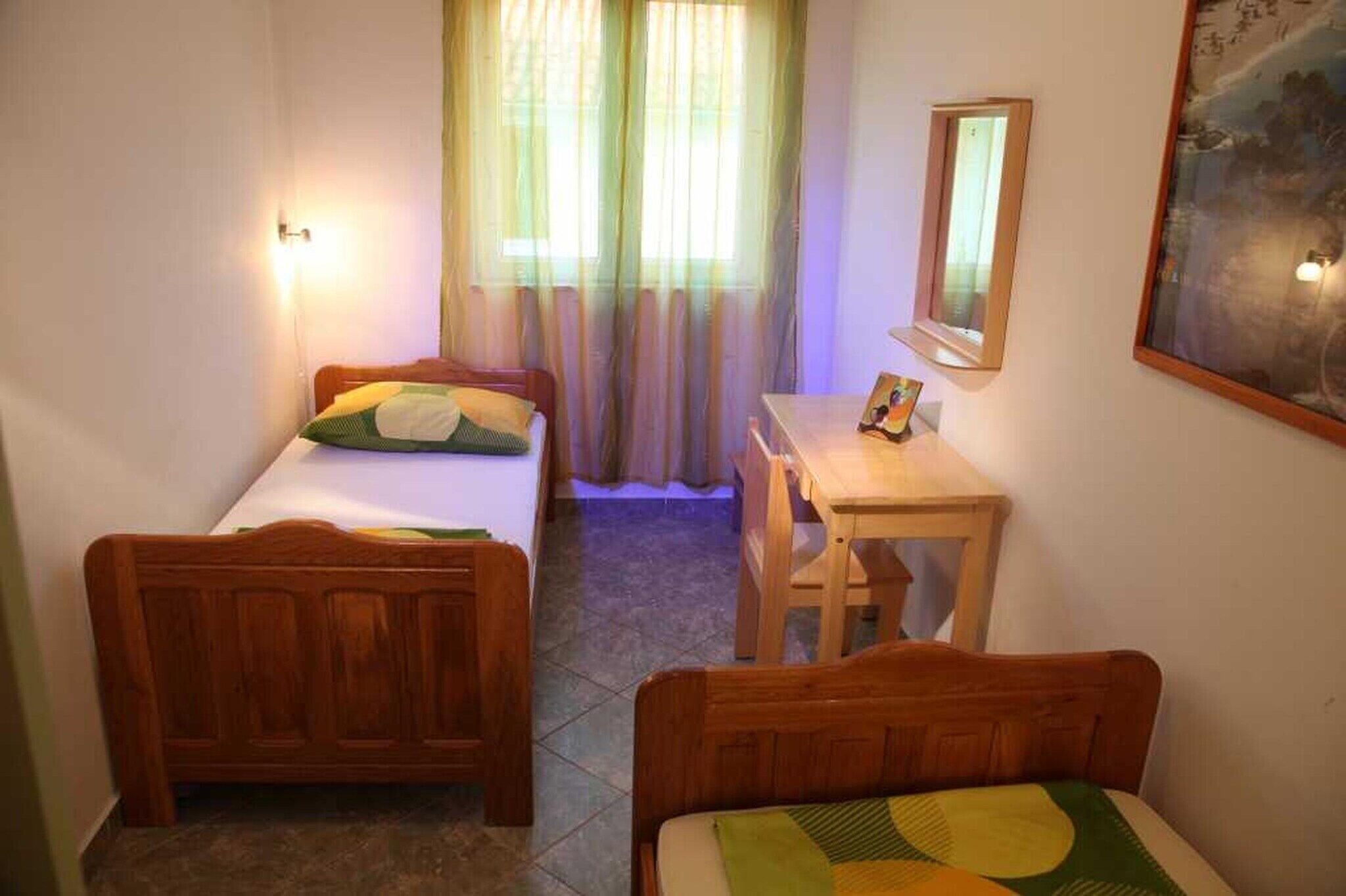 Una stanza piccola con due letti in legno, una scrivania, una sedia, uno specchio e un quadro appeso al muro.