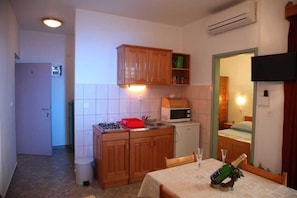 A compact kitchen with a microwave, stove, and cabinets, a dining table with a bottle, and a TV mounted on the wall. - Luxe Srima Retreat with Boat Mooring (Srima)