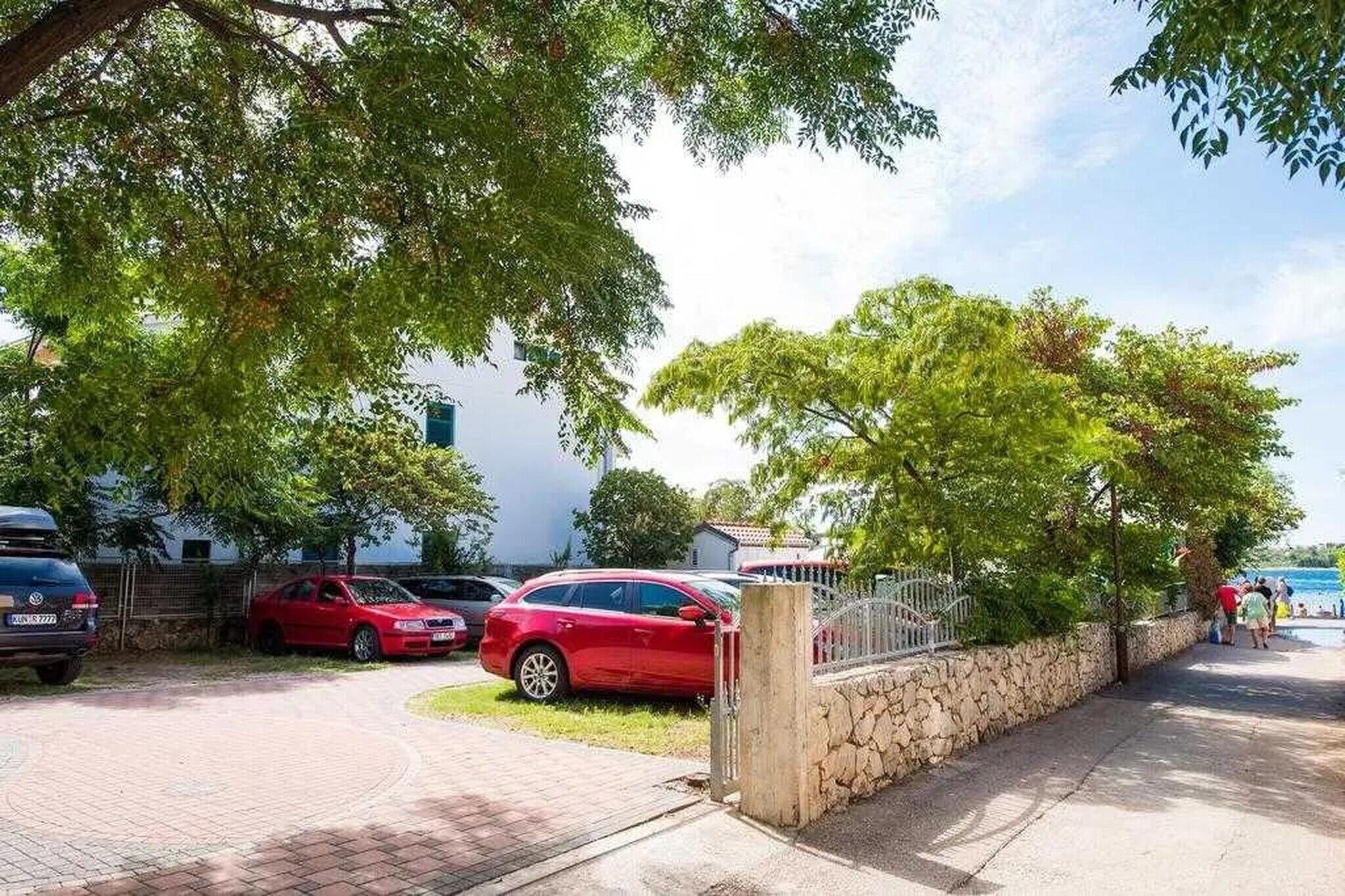 A parking area with cars, a stone wall, and a paved walkway leading to a beach.