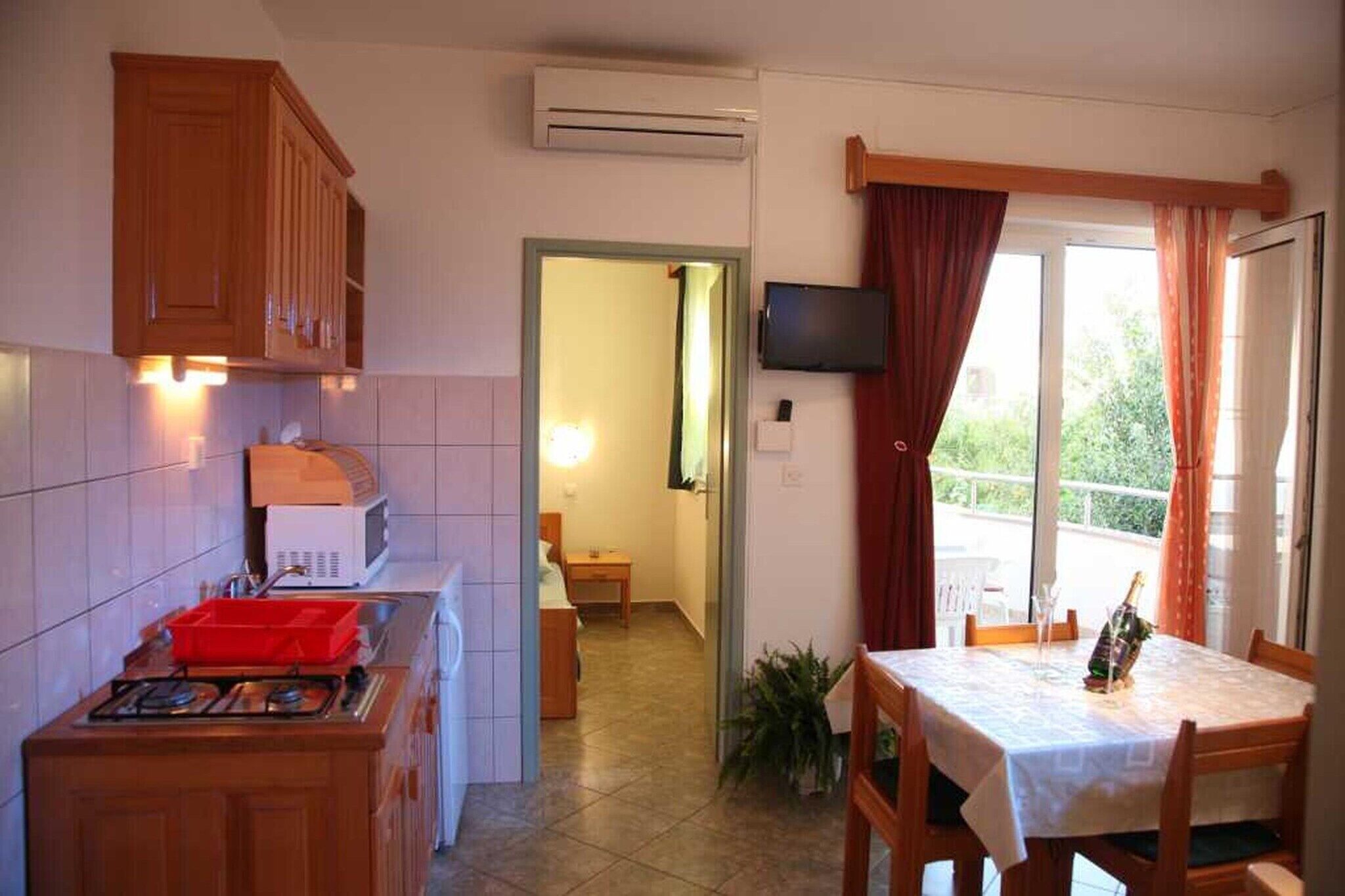 Eine kleine Küche mit Mikrowelle, Spüle und Schränken, die auf einen Balkon mit Tisch und Fernseher führt.