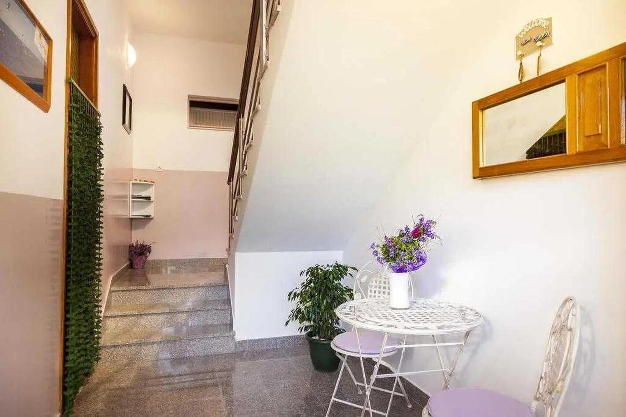 Eine Treppe führt zu einer Zwischenebene mit einer weißen Wand, einem kleinen Tisch mit einem Blumenstrauß und einem Spiegel an der Wand.