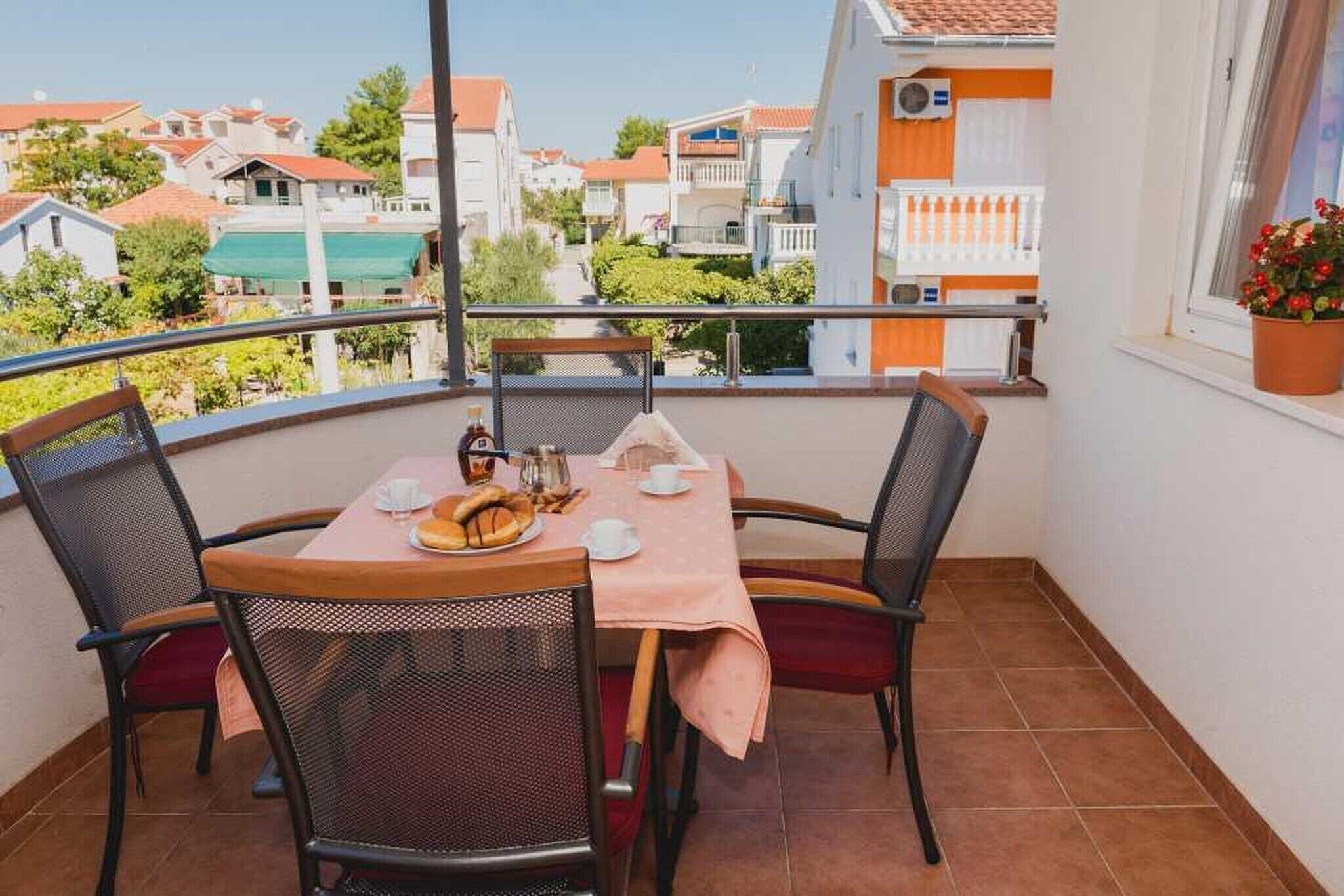 Un balcon avec une table dressée pour deux personnes, des chaises, une plante en pot et une vue sur le quartier.