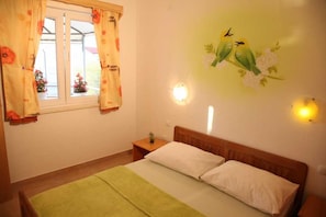 Ein Schlafzimmer mit Bett, Nachttisch, einem Fenster mit Vorhängen, Wandleuchten und einer Vogel-Wanddekoration.